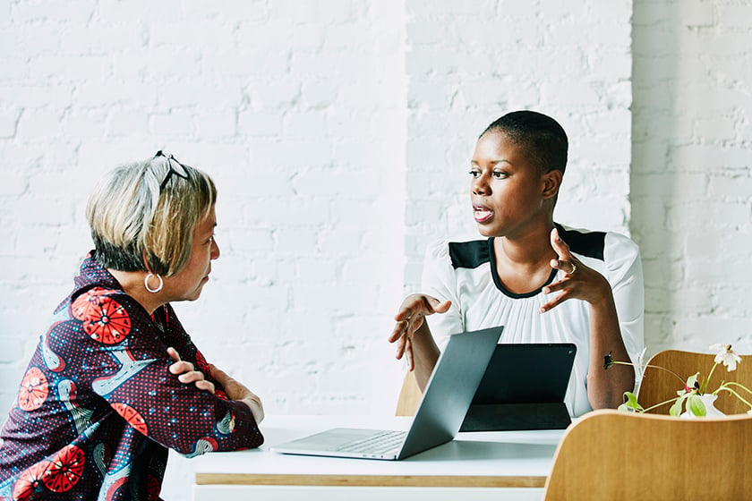 An accountant speaks with her client at a meeting room table. Both women are engaged in the in-depth conversation.