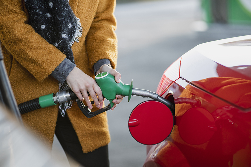 A woman uses a fuel pump to put petrol into a red car.