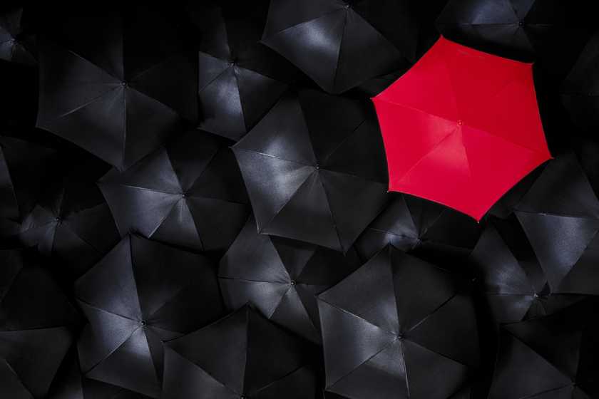 Red umbrella standing out from a group of black umbrellas