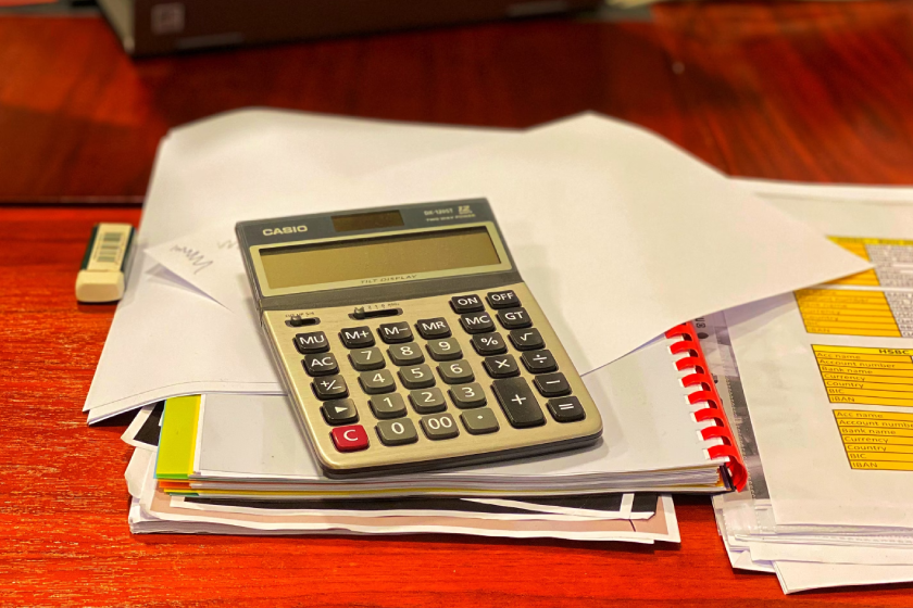Photo of a calculator sitting on top a medium stack of notebooks and documents