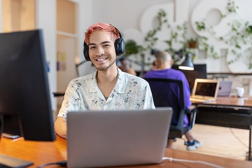 Photo of a young office worker. He has pink hair and is wearing headphones.