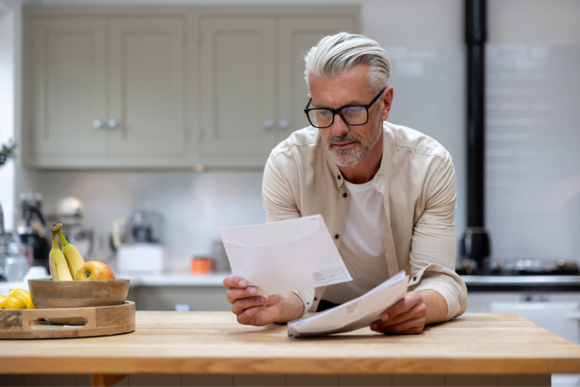 Mature man leaning against a kitchen bench top reading mail