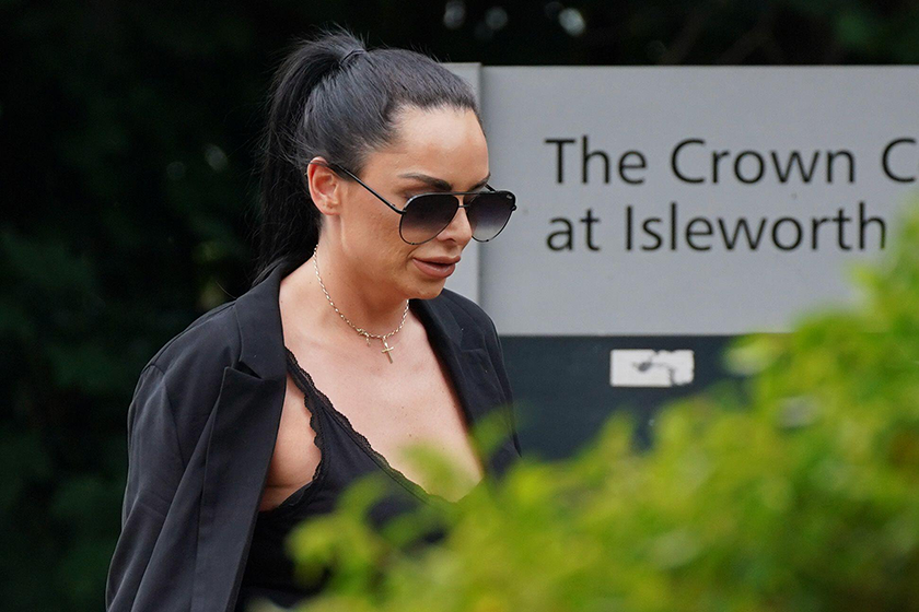 A woman walks past a sign that reads 'The Crown Court at Isleworth'. She wears dark glasses and black clothing, and is looking at the ground. 